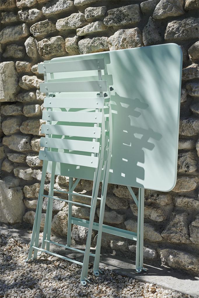 Table d’extérieur bistrot pliée avec ses chaises contre un mur prête à être utilisées ou rangées