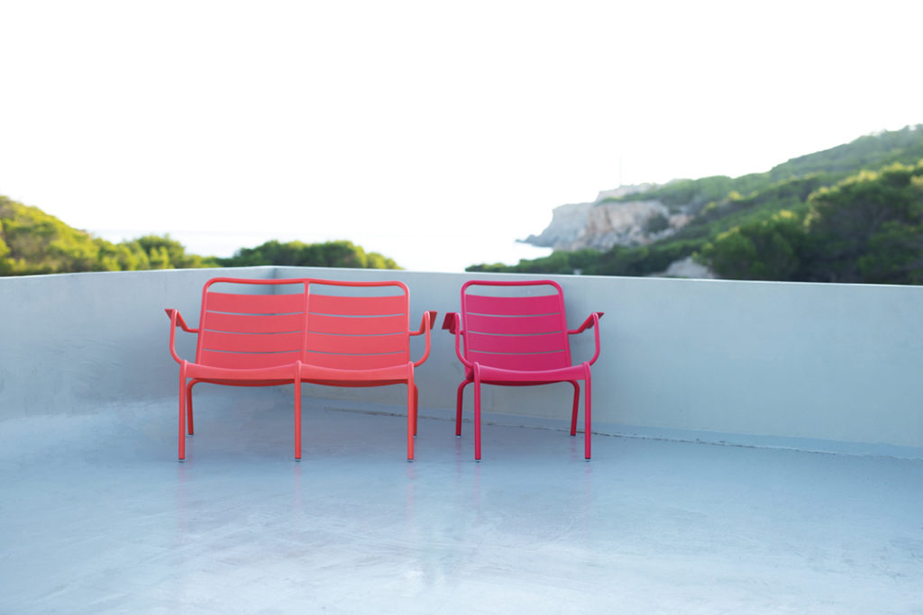 Banc bas Luxembourg avec accoudoir posé sur une terrasse de béton au soleil vue montagnes et mer