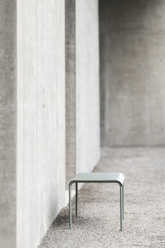 Une table de bar August se trouve devant un mur en béton.