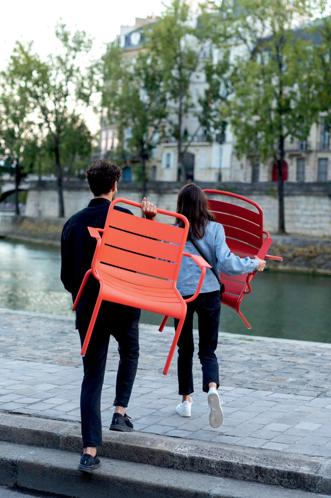 Chaise d’exterieur avec accoudoir Luxembourg transporté par des gens en bord de Seine au soleil