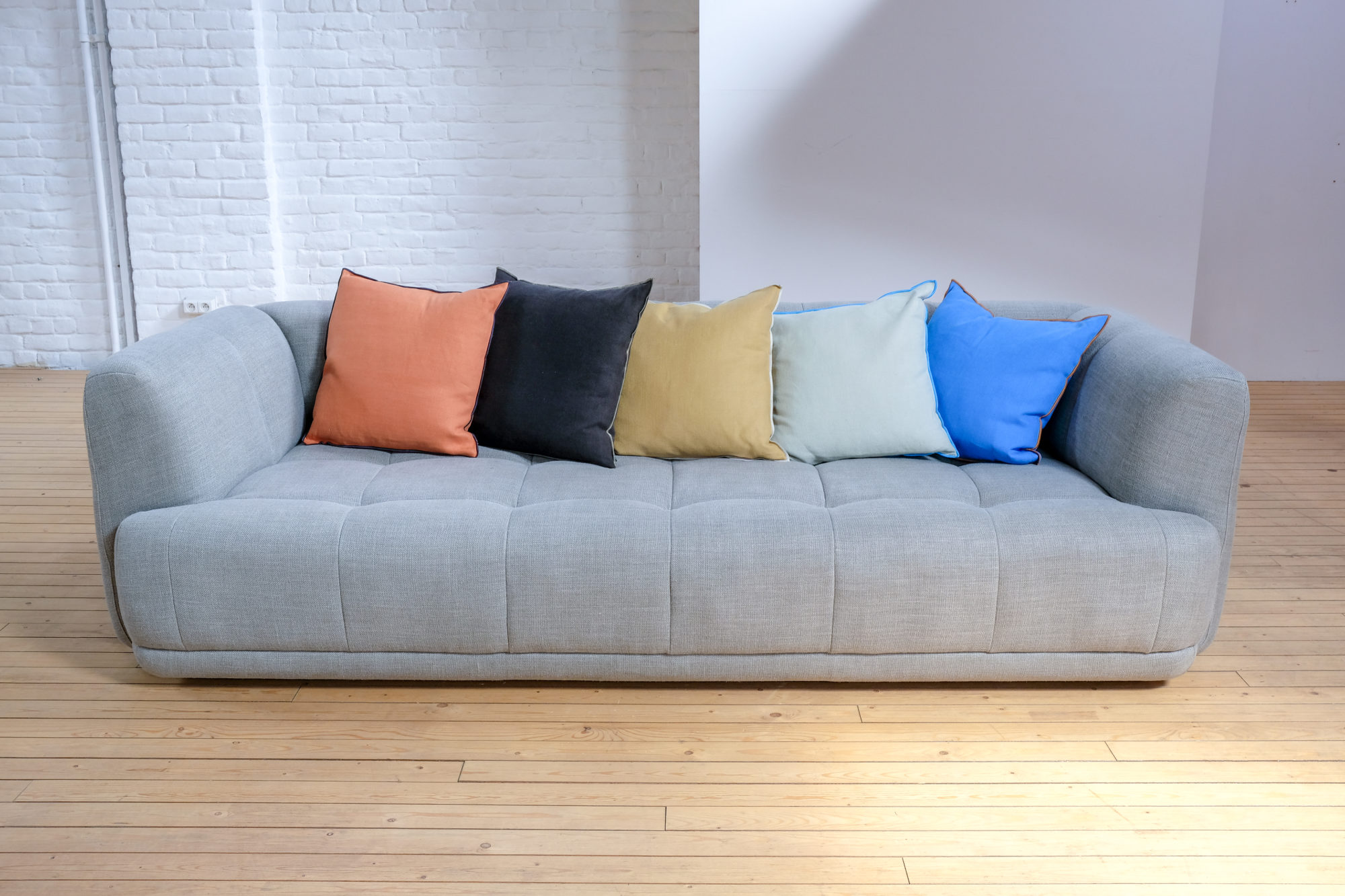 Un canapé avec des oreillers colorés à côté d'une prise sur un parquet.