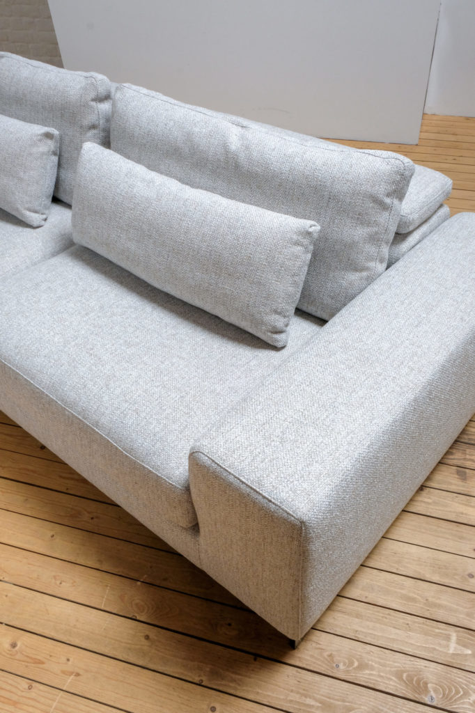 Un canapé gris avec des oreillers sur un parquet.