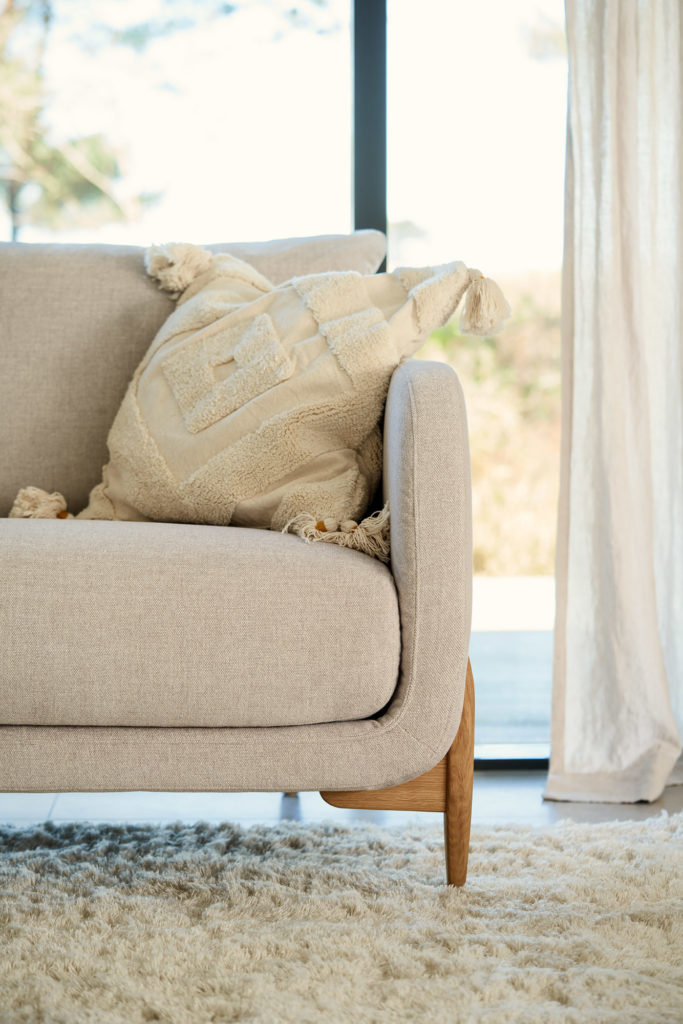 Canapé Jenny, 3 places assise sur un canapé beige devant une fenêtre.