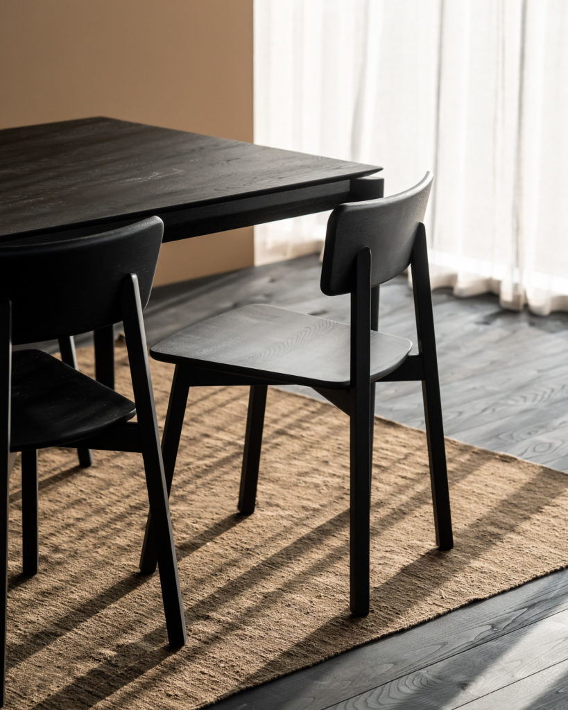 Une table à manger noire et des chaises Chaise Casale en chêne noir devant une fenêtre.