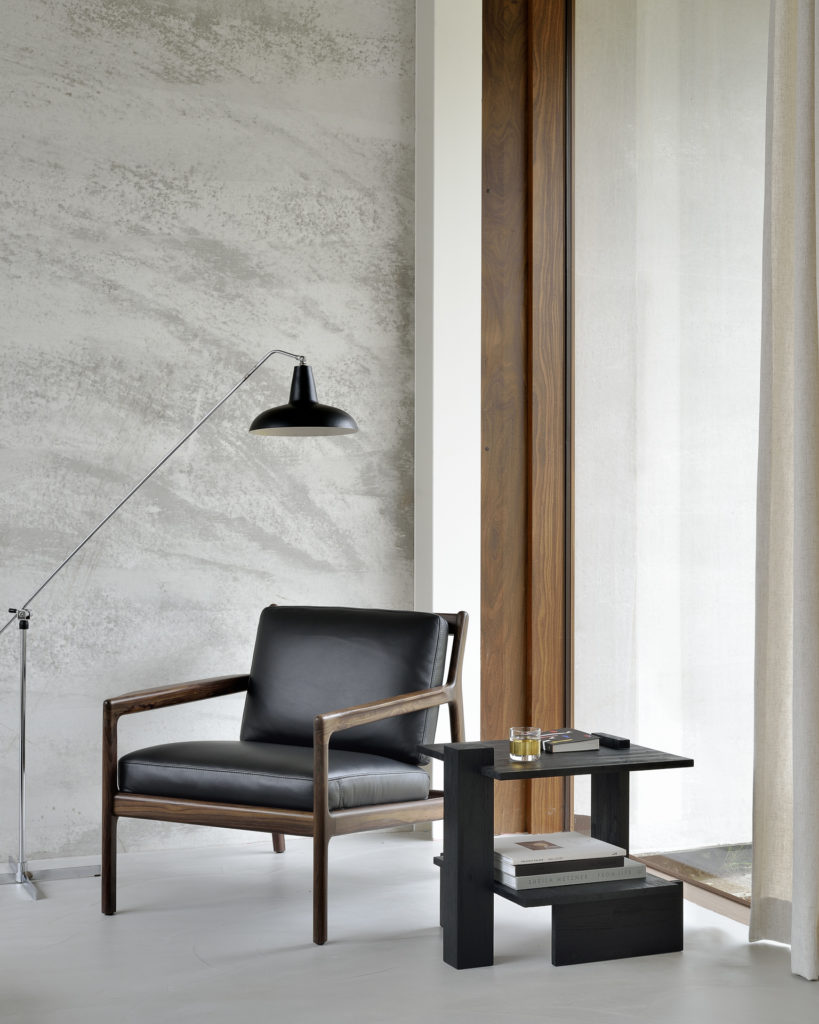 Une chaise noire et une table d'appoint Abstract en teck dans une pièce avec une grande fenêtre.