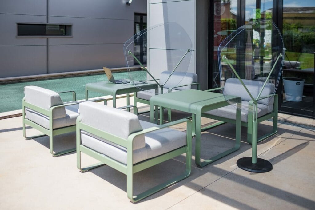 Patio extérieur avec mobilier Fauteuil Bellevie moderne vert et blanc et écrans de protection transparents, posé sur un sol carrelé contre un bâtiment.