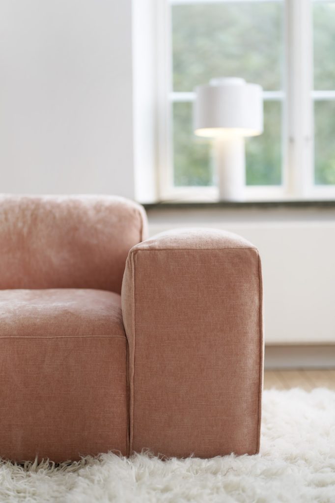 Un modèle de canapé rose qui repose devant une fenêtre.