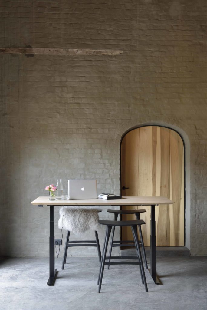 Bureau Bok d’Ethnicraft avec structure en métal noir, entourée de quatre tabourets en chêne noir Osso et sur lequel se trouve un bureau dans un intérieur rustique.