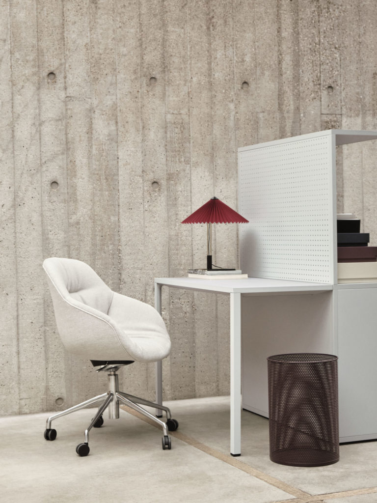 Chaise AAC 155 d’Hay en tissu blanc rembourré, avec base en aluminium à roulettes devant un bureau de type industriel.