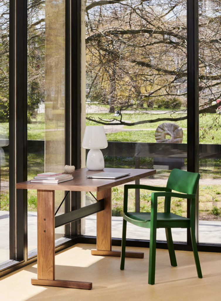 Une chaise verte confortable se trouve à côté d’un bureau dans une pièce dotée de grandes fenêtres.