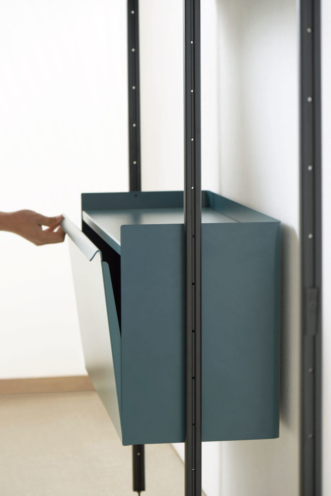 Une personne tient une boîte bleue Dressing modulable Pier System 1072 sur une étagère.