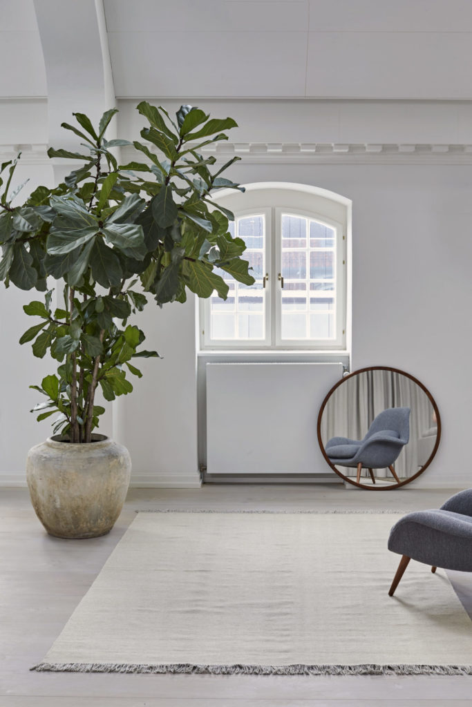 Un salon blanc avec une grande plante en pot et un tapis Tapis Escape Kelim avec franges.