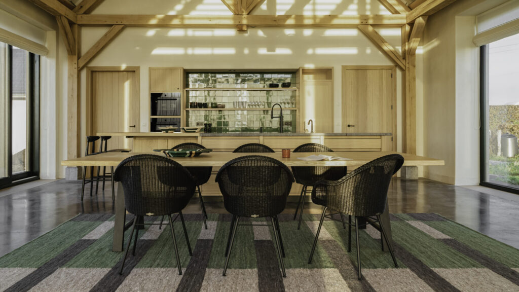 La cuisine et la salle à manger sont dotées de poutres en bois rustiques, d'une table Albert classique entourée de six chaises noires élégantes, d'un îlot avec tabourets de bar et d'un mur d'étagères et d'armoires. La lumière naturelle y pénètre, ajoutant une ambiance chaleureuse et un charme pratique à l'espace.