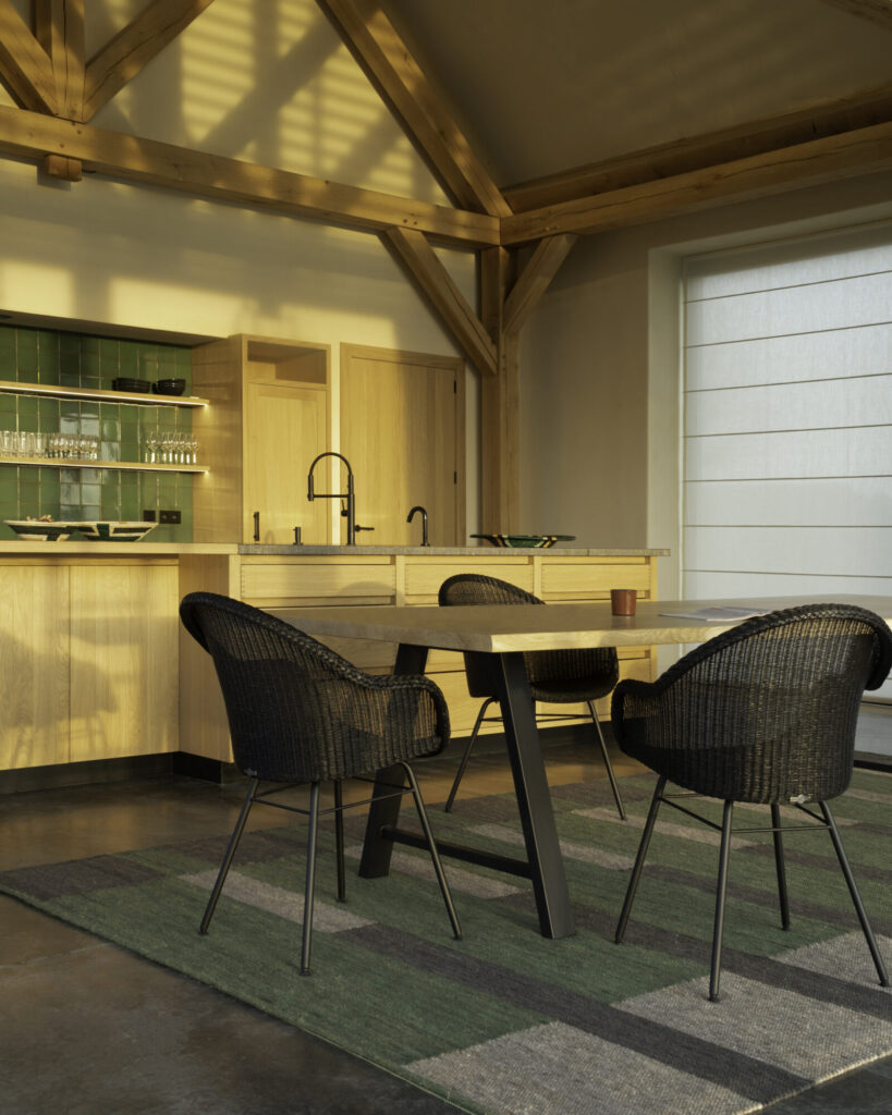 Une cuisine moderne avec des armoires en bois et une table Albert ainsi que quatre chaises tressées. La lumière du soleil pénètre à travers une fenêtre, créant une ambiance chaleureuse et accueillante.