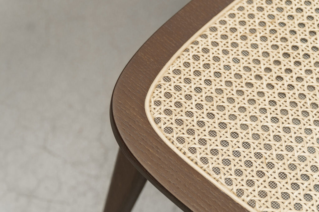 Gros plan de la chaise en bois Chaise Titus dotée d'un siège en rotin tressé, vue sous un angle sur un sol gris texturé.