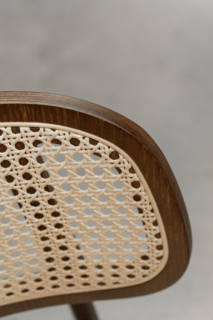 Gros plan de la Chaise Titus, mettant en valeur sa structure en bois et son dossier en osier tressé, placés sur un fond neutre.