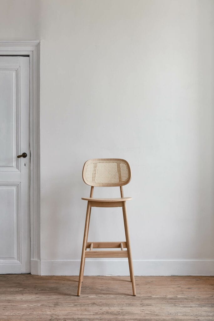 Une chaise en bois devant une porte dans une pièce vide, surmontée d'un tabouret.
