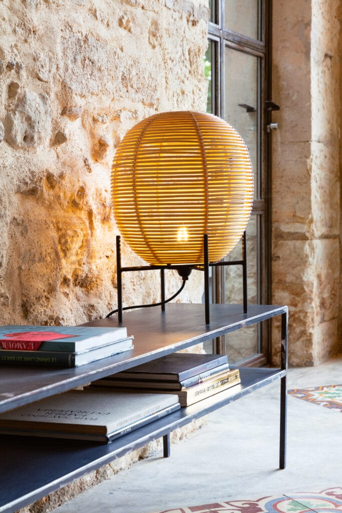 Une table en bois avec une lampe et des livres dessus, éclairée par une Lampe Sari.