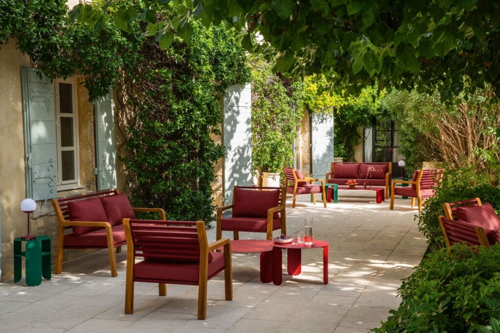 Un coin salon extérieur serein avec des chaises et des tables LUNA CHAIR rouges, entouré d'une verdure luxuriante et de plantes grimpantes.