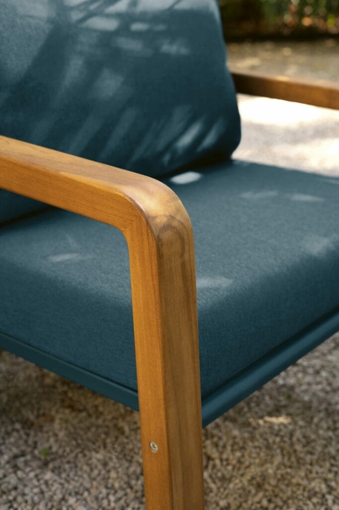Gros plan d'un fauteuil Somerset avec accoudoir en bois et coussin bleu, placé à l'extérieur.