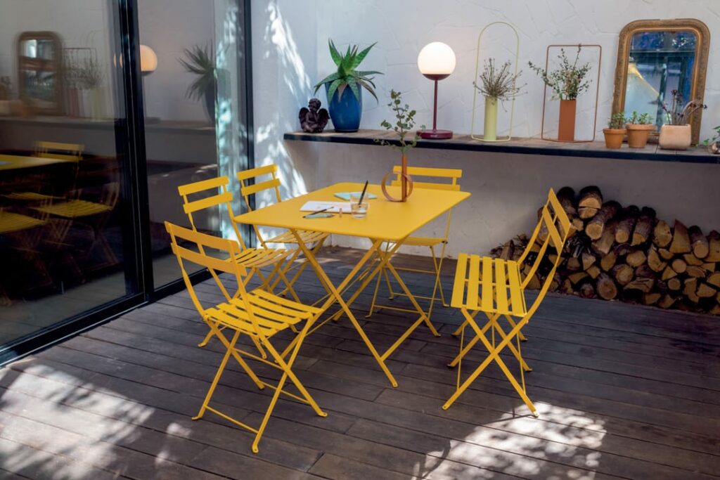 Une table et des chaises en métal Chaise Bistro jaune sur une terrasse en bois.