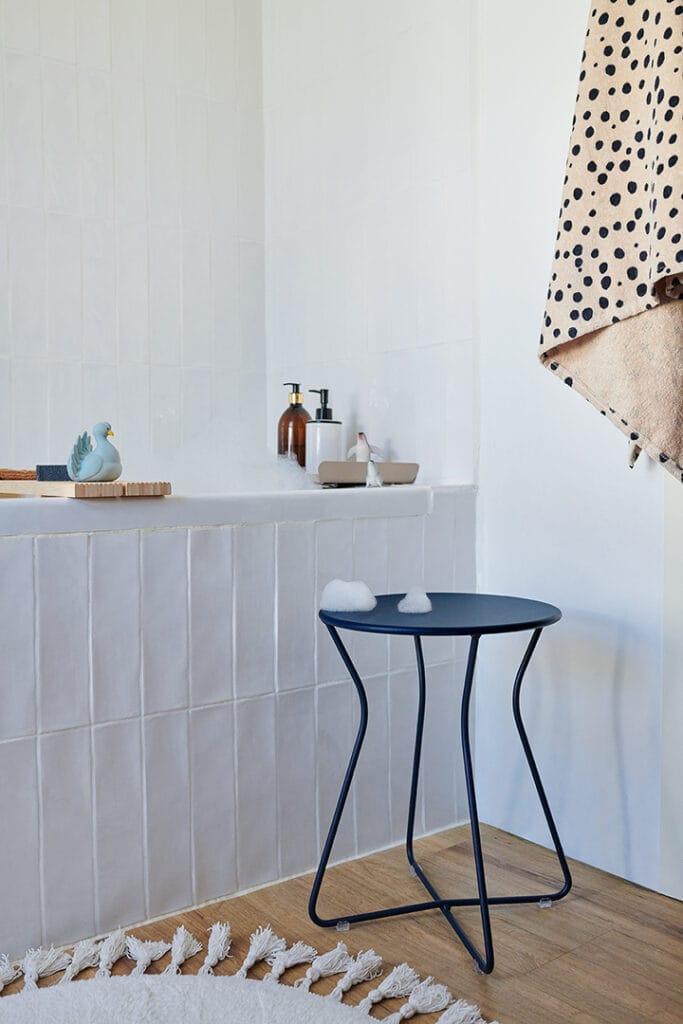 Une salle de bain avec un tapis, une baignoire et un Tabouret Cocotte.
