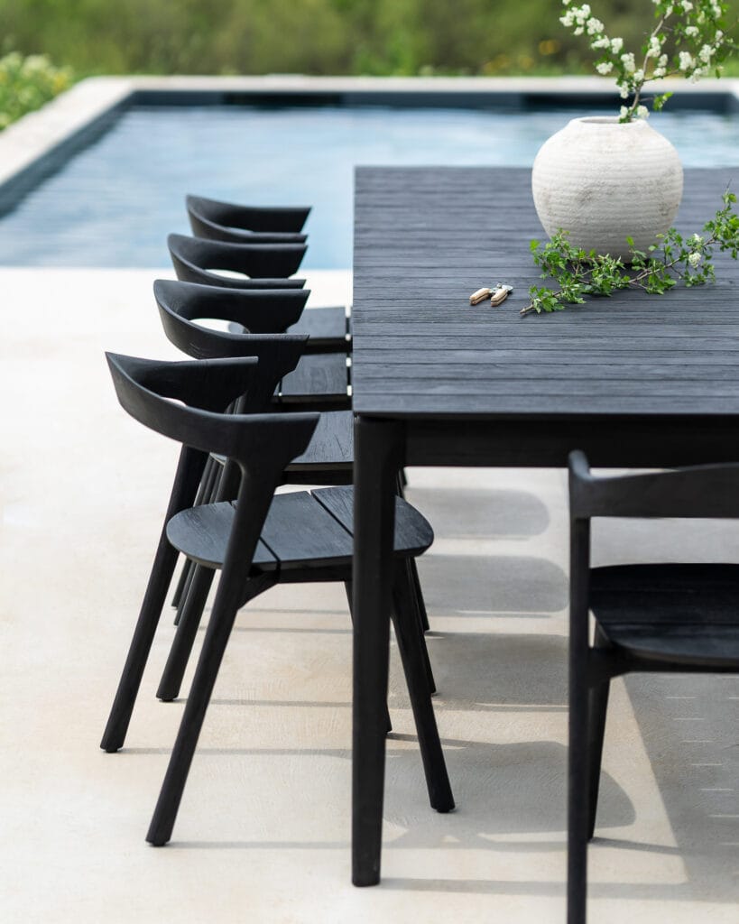 Une table à manger noire et des **chaises de jardin Bok en teck noir** près d'une piscine.