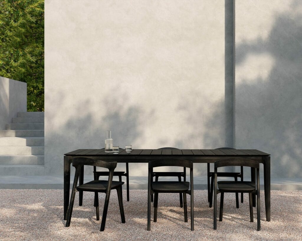 Une chaise de jardin Bok en teck noir et des chaises devant un mur en pierre.