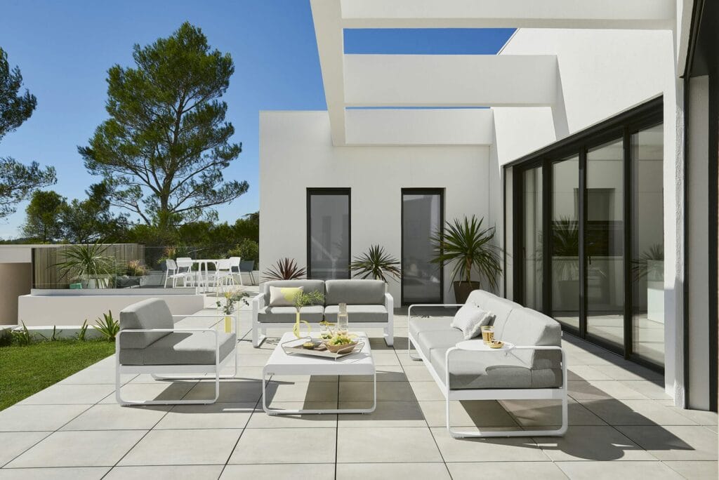 Patio moderne avec mobilier d'extérieur comprenant des canapés et une Grande table basse Bellevie, entouré d'une verdure luxuriante, par une journée ensoleillée.