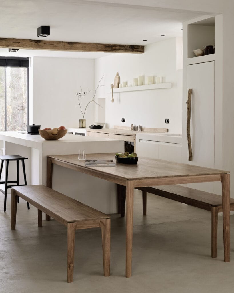 Un Canapé Mellow, une table et des bancs en bois module 1 place ajoutent une touche de chaleur douce à cette cuisine blanche.