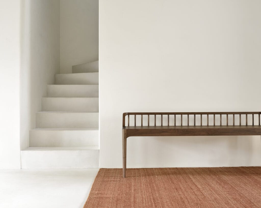 Un banc Tapis Kilim Nomad trône élégamment à côté d'un escalier dans une pièce blanche.