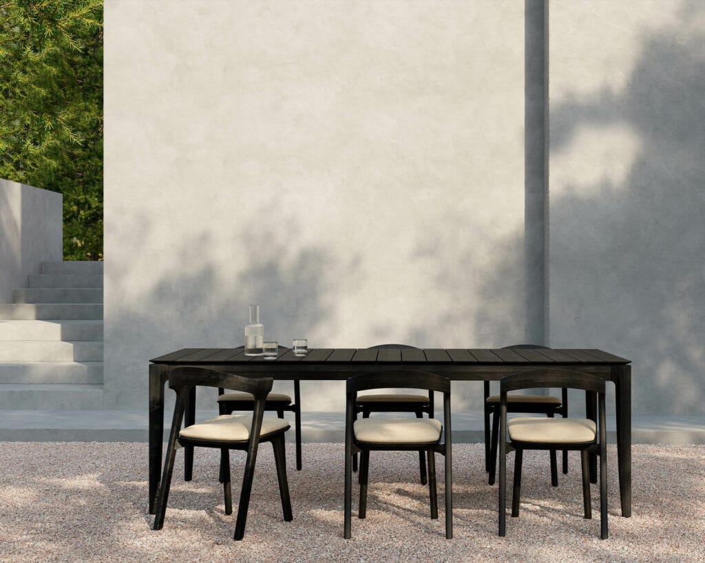 Un bok chaise de jardin, une table à manger en teck noir et des chaises chaise de jardin devant un mur en pierre.