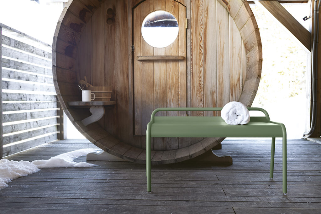 Un Banc compact Luxembourg se trouve devant un tonneau en bois.