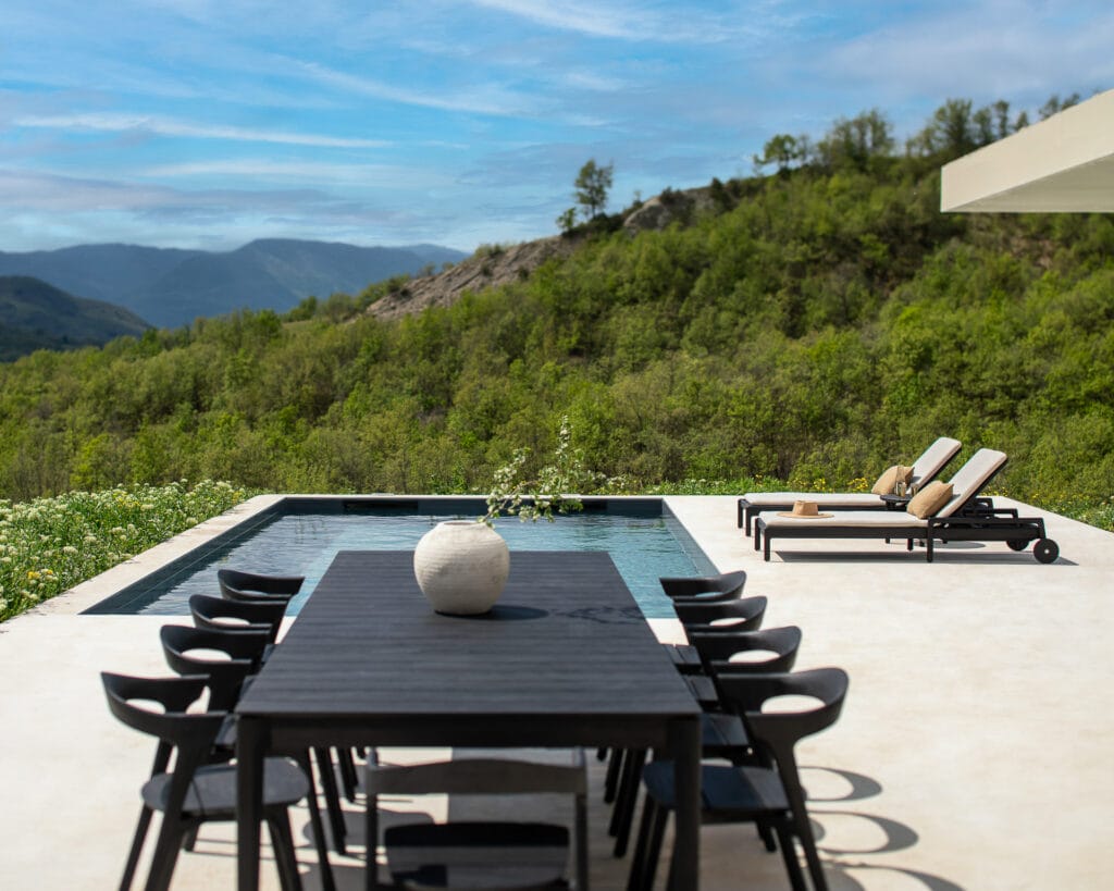 Une table de jardin Bok en teck noir et des chaises en teck noir sur une terrasse avec vue sur les montagnes.