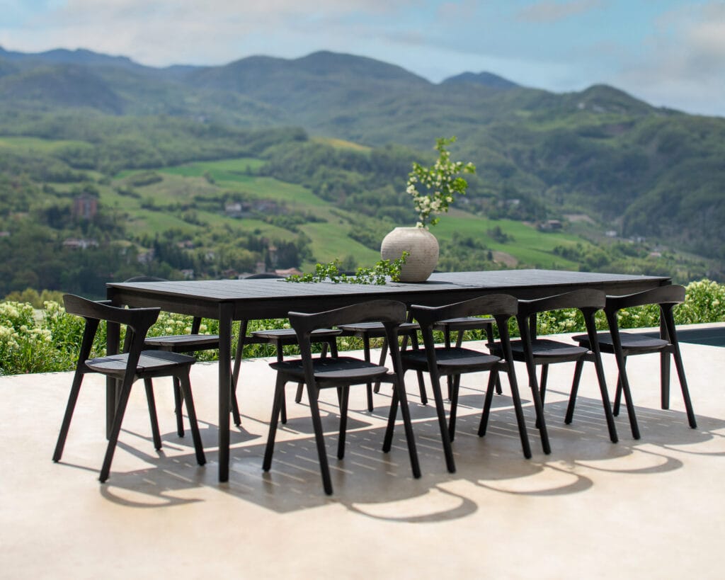 Table de jardin Bok en teck noir sur un patio avec des montagnes en arrière-plan.