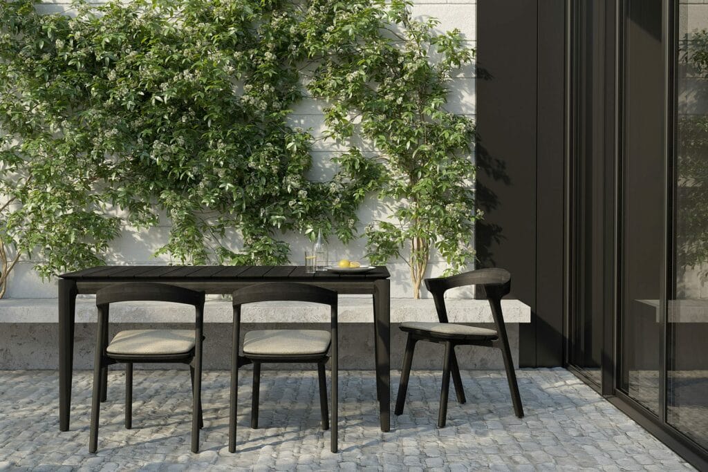 La Table de jardin Bok en teck noir est devant un mur vert.