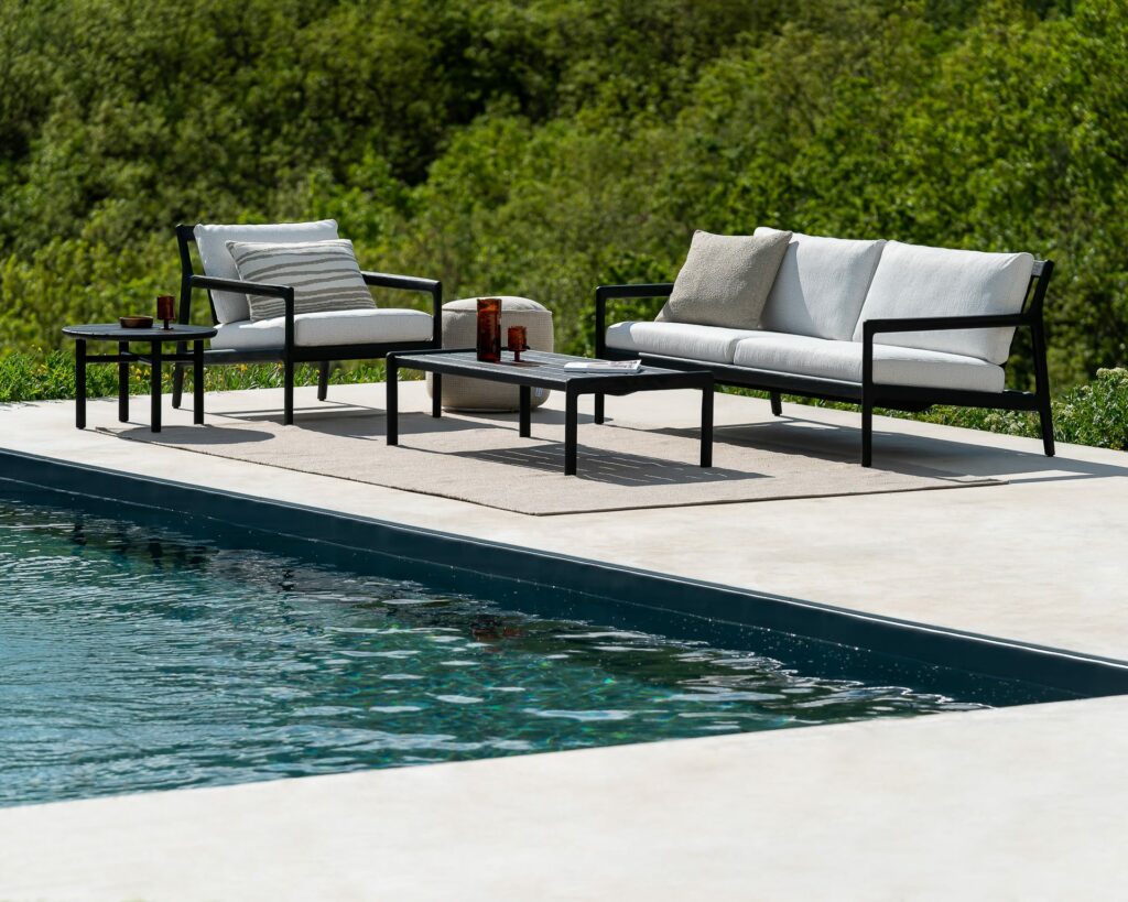 Un ensemble de Canapé de jardin Jack en teck noir - Mobilier d'extérieur 2 places au bord d'une piscine.