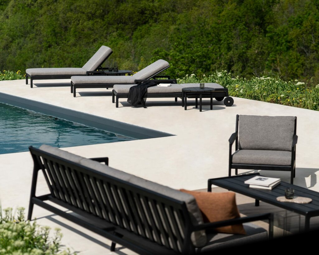 Un ensemble de chaise longue de jardin Jack en teck noir près d'une piscine.