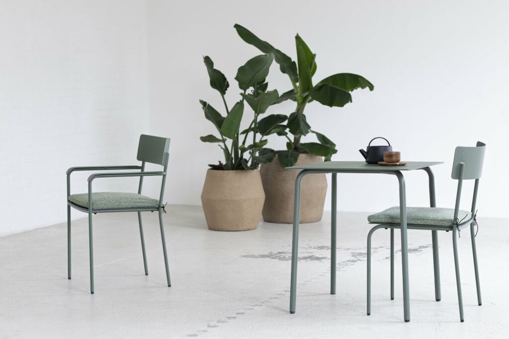 Deux chaises avec accoudoirs August et une table dans une pièce avec plantes en pot.