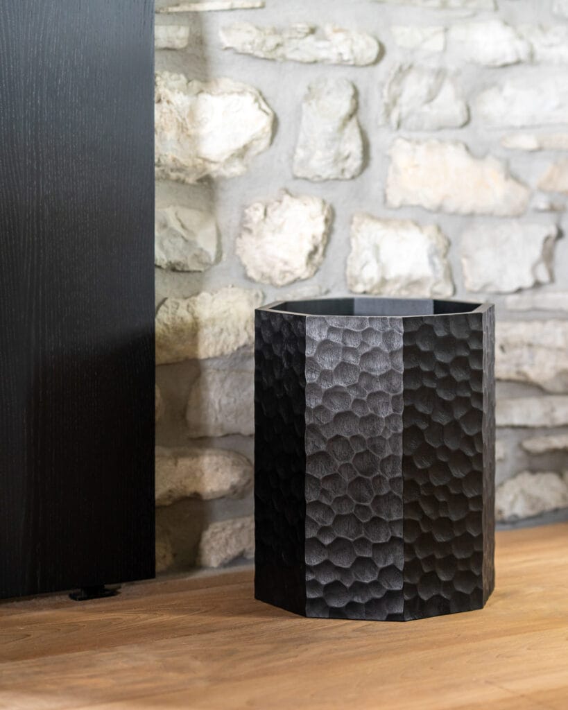 Une jardinière en métal noir posée sur un sol en pierre, rappelant une Corbeille à papier Hachée.