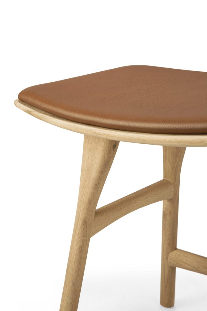 Un tabouret en Chêne naturel vernis avec une assise en cuir marron.
