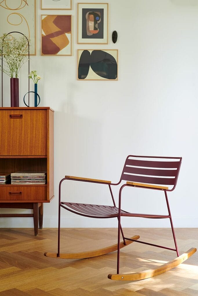 Intérieur moderne comprenant un rocking chair surprenant, une armoire en bois et des œuvres d'art abstraites sur un mur minimaliste.