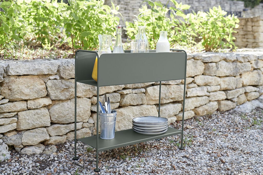 Un chariot Picolino Cache-pot vert avec de la vaisselle devant un mur de pierre.