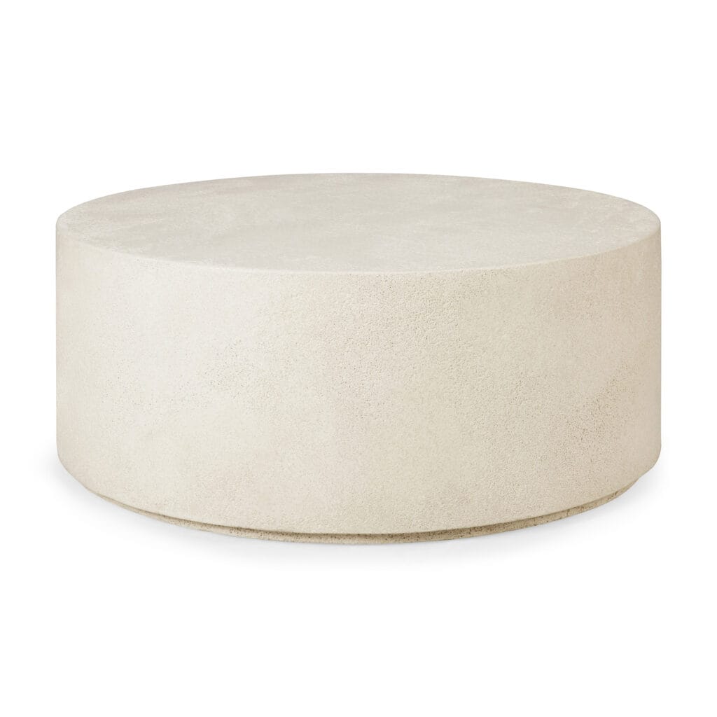 Une table basse ronde en béton sur un fond blanc cassé.