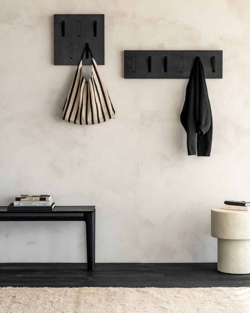 Un Porte-manteau Utilitile avec un porte-manteau mural en chêne teinté noir, sur lequel est accroché un sac.