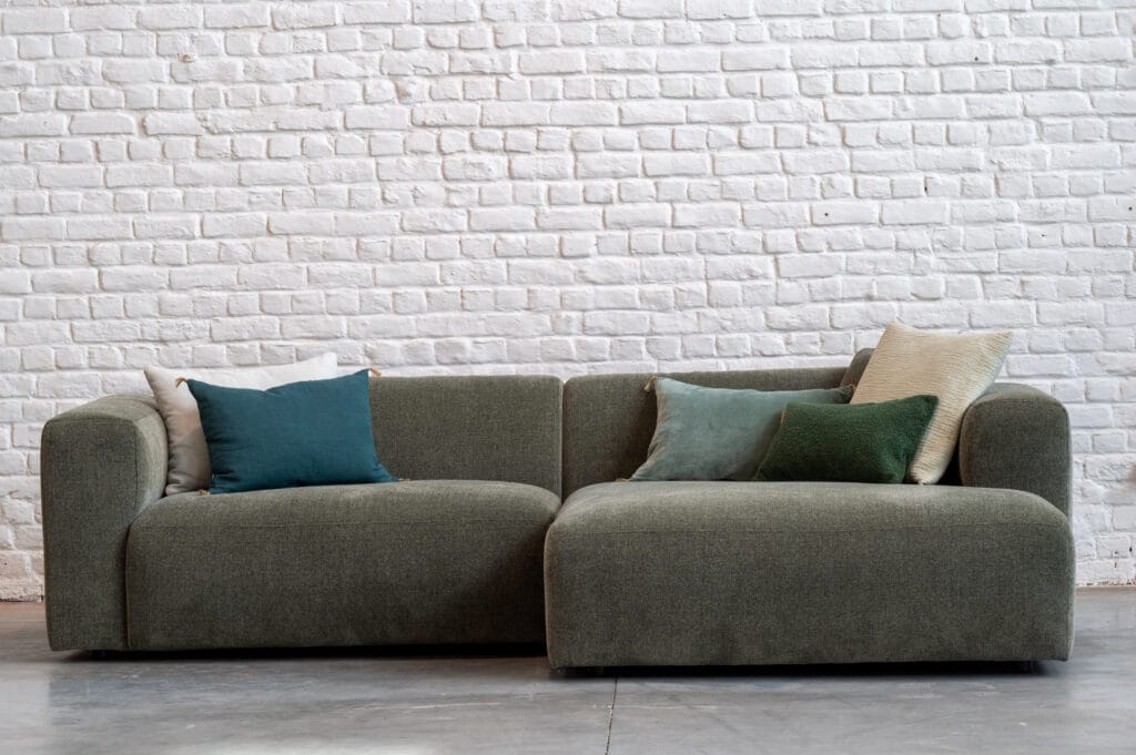 Canapé Annie, tissu Stipa était assis sur un canapé vert devant un mur de briques blanches.
