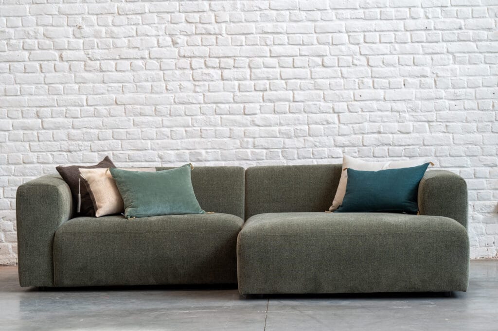 Un Canapé Annie vert devant un mur de briques blanches.