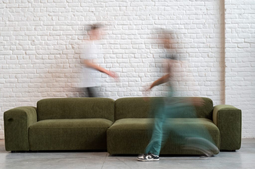 Deux personnes se promenant à côté d’un Canapé Edda vert vif en tissu Moss.