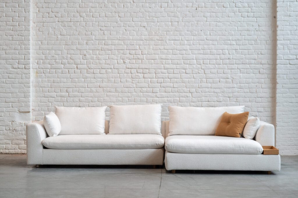 Un Canapé Milou blanc, recouvert de tissu Heather, devant un mur de briques.