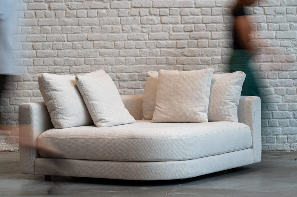 Un Canapé Stone en tissu Wicker, placé devant un mur de briques.